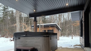 A covered outdoor area with a hot tub, a wooden deck, and a view of a cabin in a snowy forest. - OFF-PISTE VBN - LUXURY - MODERN - SPA (St-Raymond)