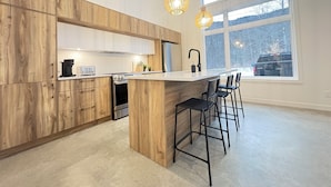 A modern kitchen with wooden cabinets, a central island, bar stools, and large windows. - OFF-PISTE VBN - LUXURY - MODERN - SPA (St-Raymond)