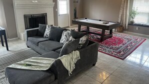 Una sala de estar con un sofá gris, una mesa de billar, una chimenea y una alfombra roja.