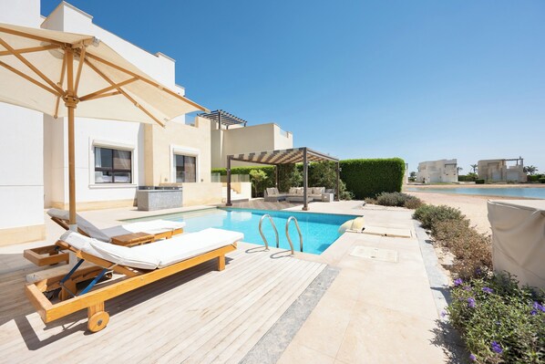 Un área de piscina moderna al aire libre con sillones de descanso y una pérgola.