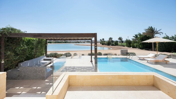 Un espace piscine agrémenté d’une pergola, de chaises longues et offrant une vue sur la plage.