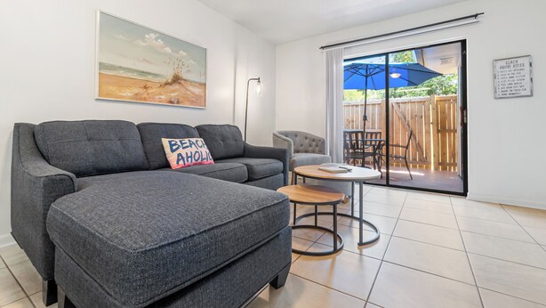 Un salon moderne avec un canapé gris, une petite table ronde et un tableau représentant une scène de plage.