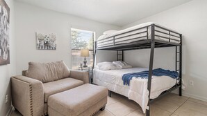 Une chambre avec un lit superposé, un canapé, une petite table avec une lampe et une fenêtre avec des stores.