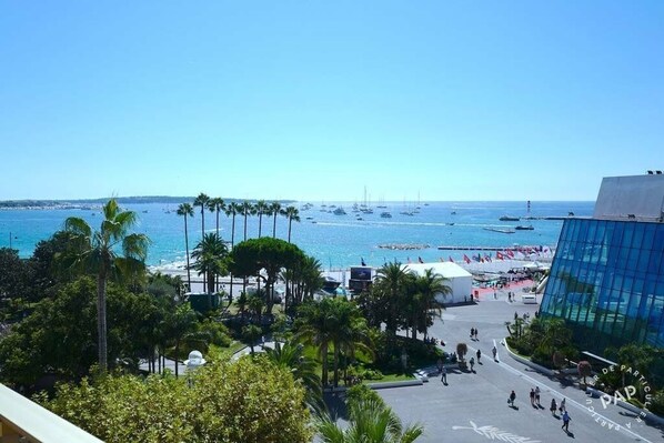A coastal view with a clear sky, palm trees, and a modern building with a glass facade.