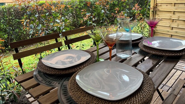 An outdoor dining area with wooden benches and woven placemats, surrounded by lush greenery and a stone wall. - Apartment Cannes garden 5mn close to downtown 5mm Gare plages Croisette (Cannes)