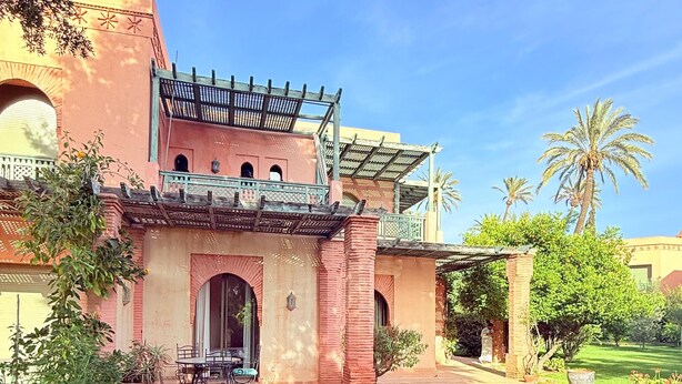 A traditional building with a covered patio, a lawn, and palm trees. - 2-bed Apartment with Garden & shared Pool- Moroccan - Modern Style (Marrakech)