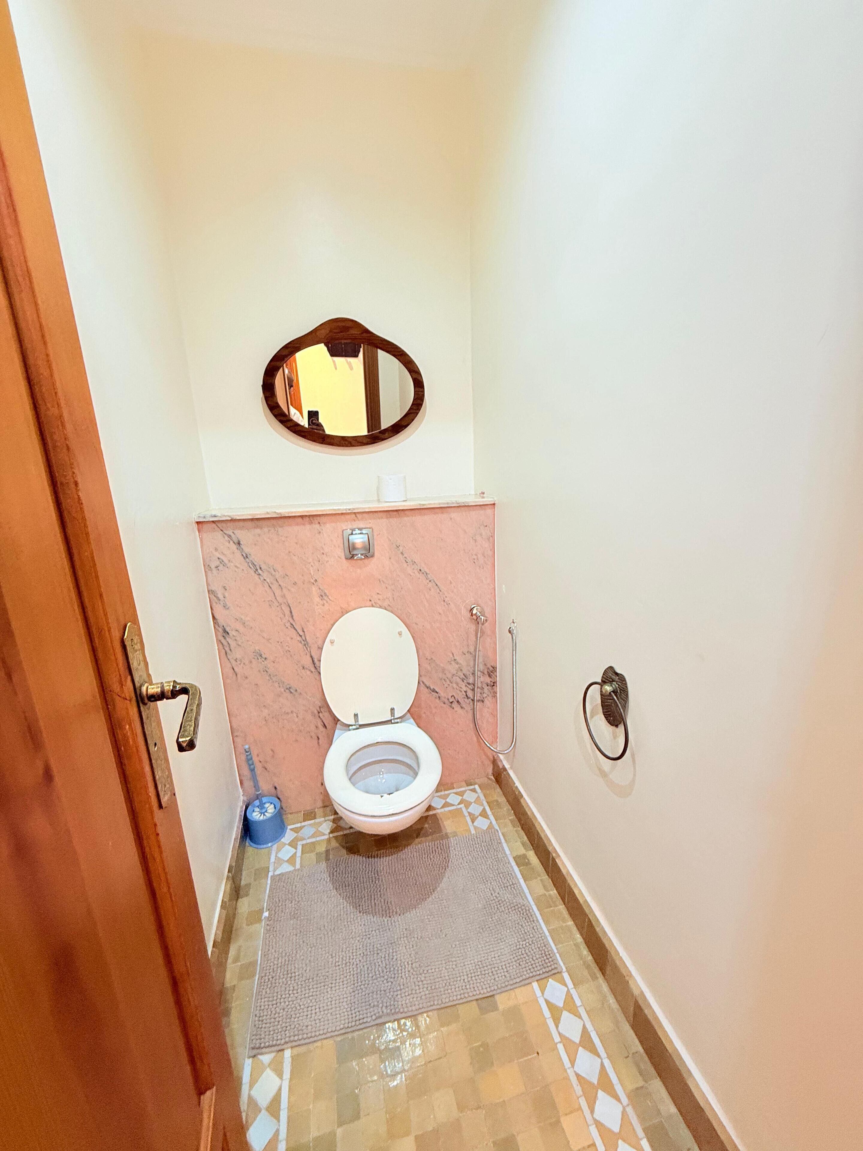 A bathroom with a toilet, a mirror, a towel mat, and a shower.