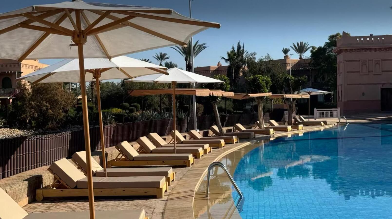 A poolside area with lounge chairs and umbrellas, a clear blue pool, and a wooden deck.