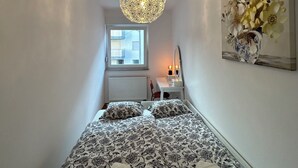 A bedroom with a bed, a desk, a chair, a window, and a hanging floral artwork. - Apartment Fran (Zagreb)