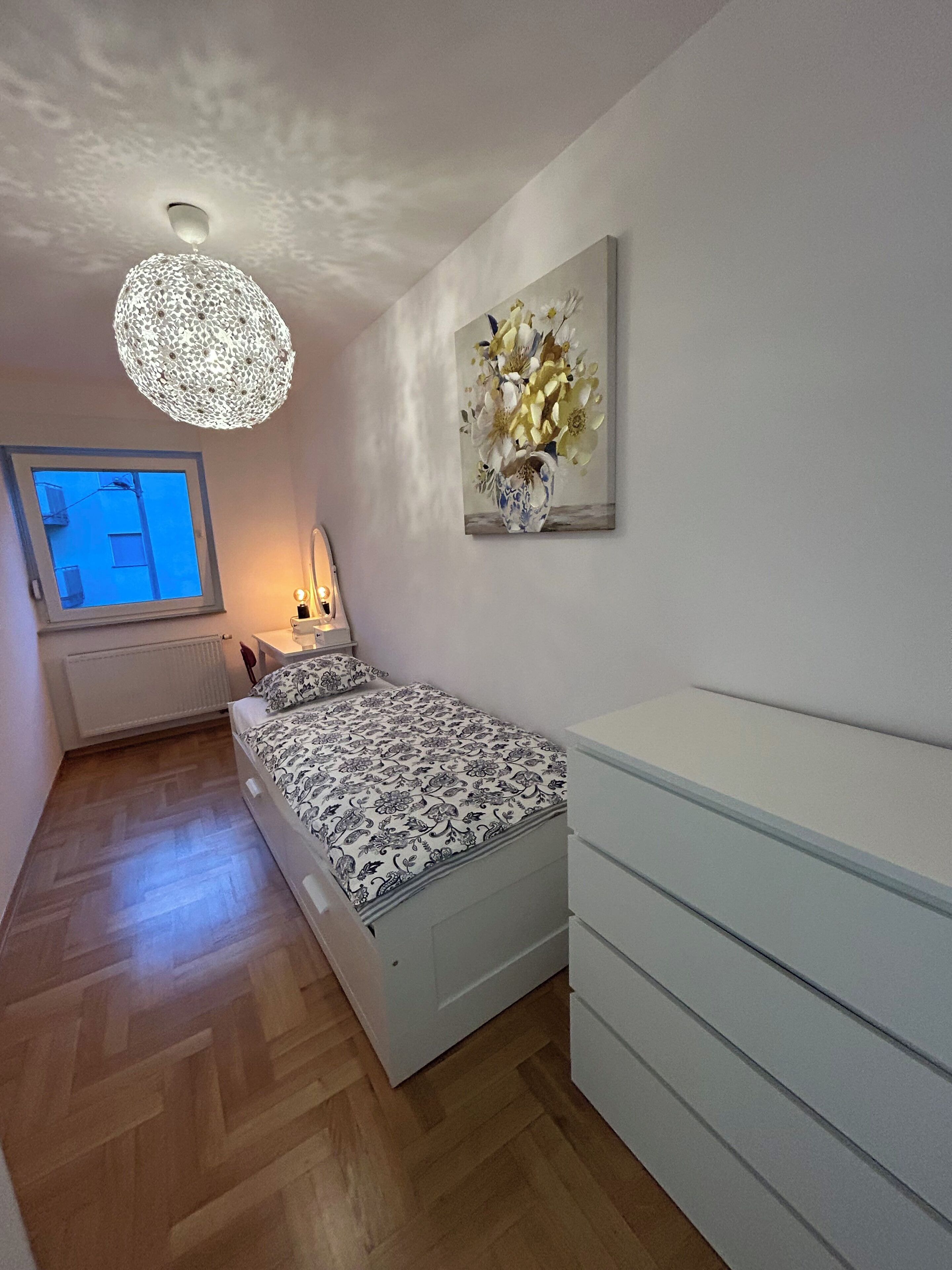 A bedroom with a bed, bedside table, lamp, and a painting on the wall.