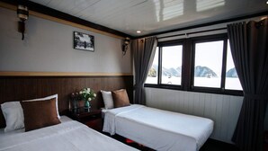 A hotel room with two beds, a wooden headboard, a nightstand with a vase of flowers, and a window with curtains. - Vietsails cruises (Bai Chay)
