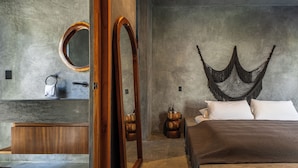 Een moderne slaapkamer met een groot bed, een houten hoofdbord, een ronde spiegel, een nachtkastje van hout en een betonnen muur.