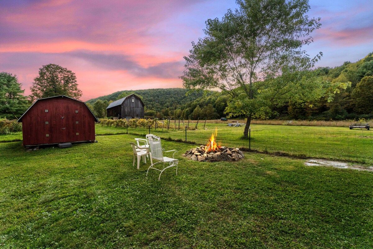 A rustic outdoor setting with a red barn, a fire pit, and white chairs.