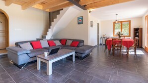 A modern living room with a gray sectional sofa, a coffee table, and a laptop. There is a staircase leading to another level, a dining area with a red tablecloth, and a wooden ceiling. - House with swimming pool and beautiful view (Lédenon)