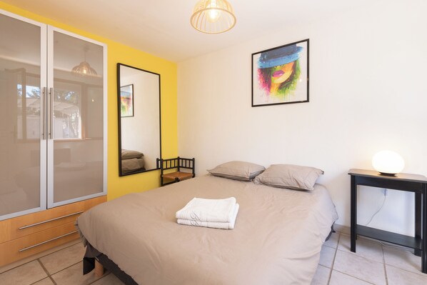 A bedroom with a bed, a wardrobe, a bedside table with a lamp, and a painting on the wall.
