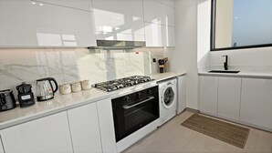 A modern kitchen with white cabinets, a gas stove, a built-in oven, a washing machine, and a coffee maker. - Private Pool | Movies in bed | No Camels (دبي)