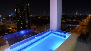A modern rooftop pool with a glass barrier, offering a city view at night. - Private Pool | Movies in bed | No Camels (دبي)