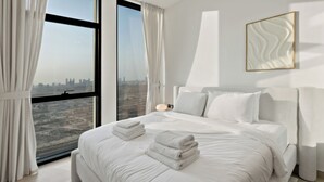 A modern hotel room with a large bed, white linens, a view of a cityscape, and a minimalist decor. - Private Pool | Movies in bed | No Camels (دبي)