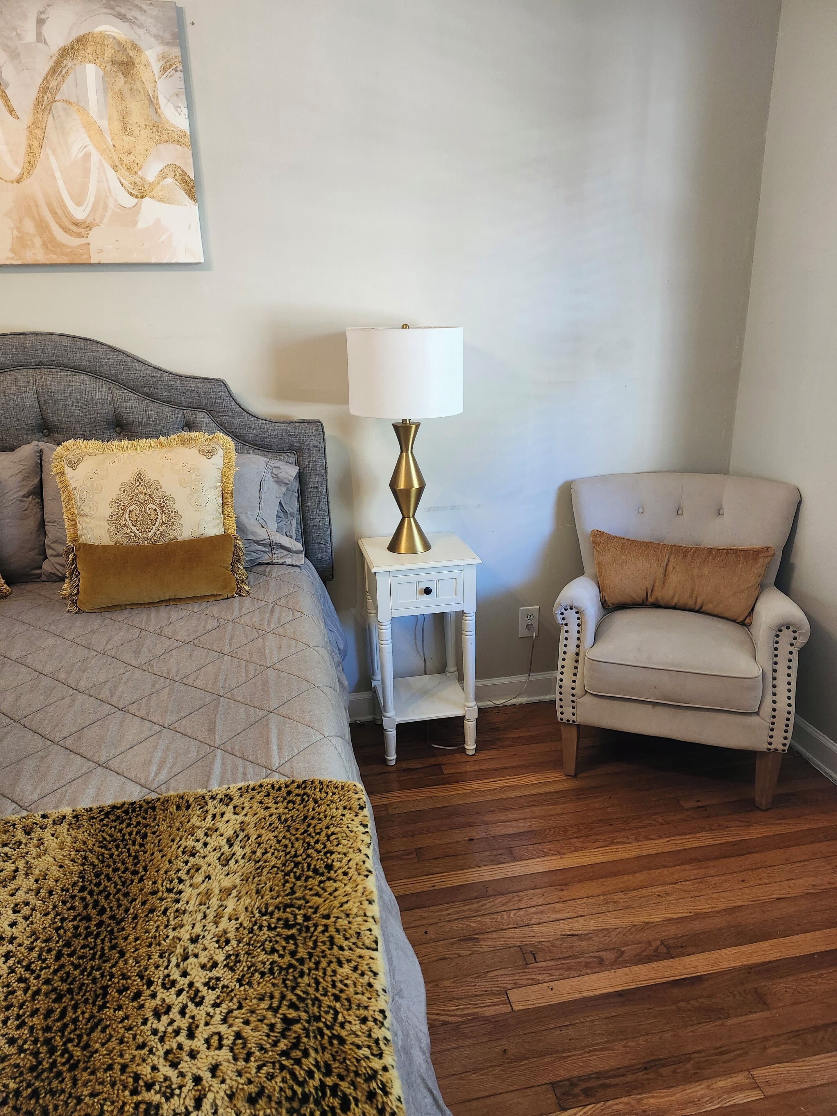 Une chambre à coucher avec un lit, une table de chevet avec une lampe, une chaise et un tableau au mur.