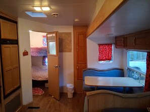 A compact RV interior with a kitchenette, a small dining area, and a bedroom with a bunk bed. - RV on 1.5 acre bluff lot overlooking lake. Fire pit, kayaks, Bike, fish and swim (Gordon)