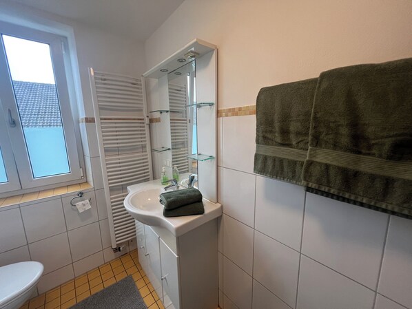 A bathroom with a white sink, a mirror, a towel hanging on the wall, and a window. - Nice quiet 2 room apartment (Ried)