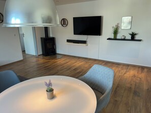 A modern living room with a round white table, two grey armchairs, a large white lamp, a flat-screen TV, a built-in fireplace, and a small plant on the table. - Nice quiet 2 room apartment (Ried)