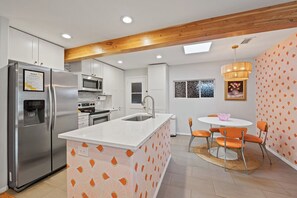 A modern kitchen with a stainless steel refrigerator, microwave, and oven. There is a white island with a sink and a dining area with orange chairs. - Zen Garden Retreat with Hiking Access, private fenced backyard (Sedona)