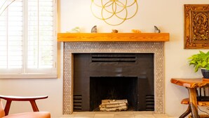 A living room with a fireplace, a dining table with a bowl of oranges, a wooden chair, and a floor lamp.