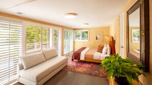 A bedroom with a bed, a sofa, a large mirror, and a potted plant.