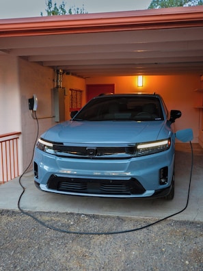 A blue car parked inside a garage with a red door, a visible power outlet, and a light fixture on the wall.
