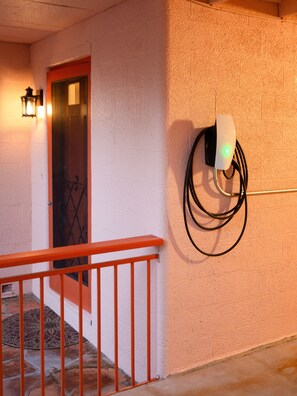 Una estación de carga para vehículos eléctricos montada en la pared, con una luz verde, una puerta roja y una barandilla de metal.