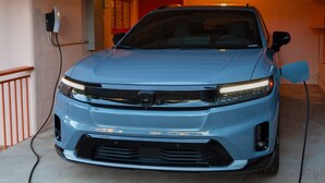A blue car parked inside a garage with a red door and a light fixture above it.