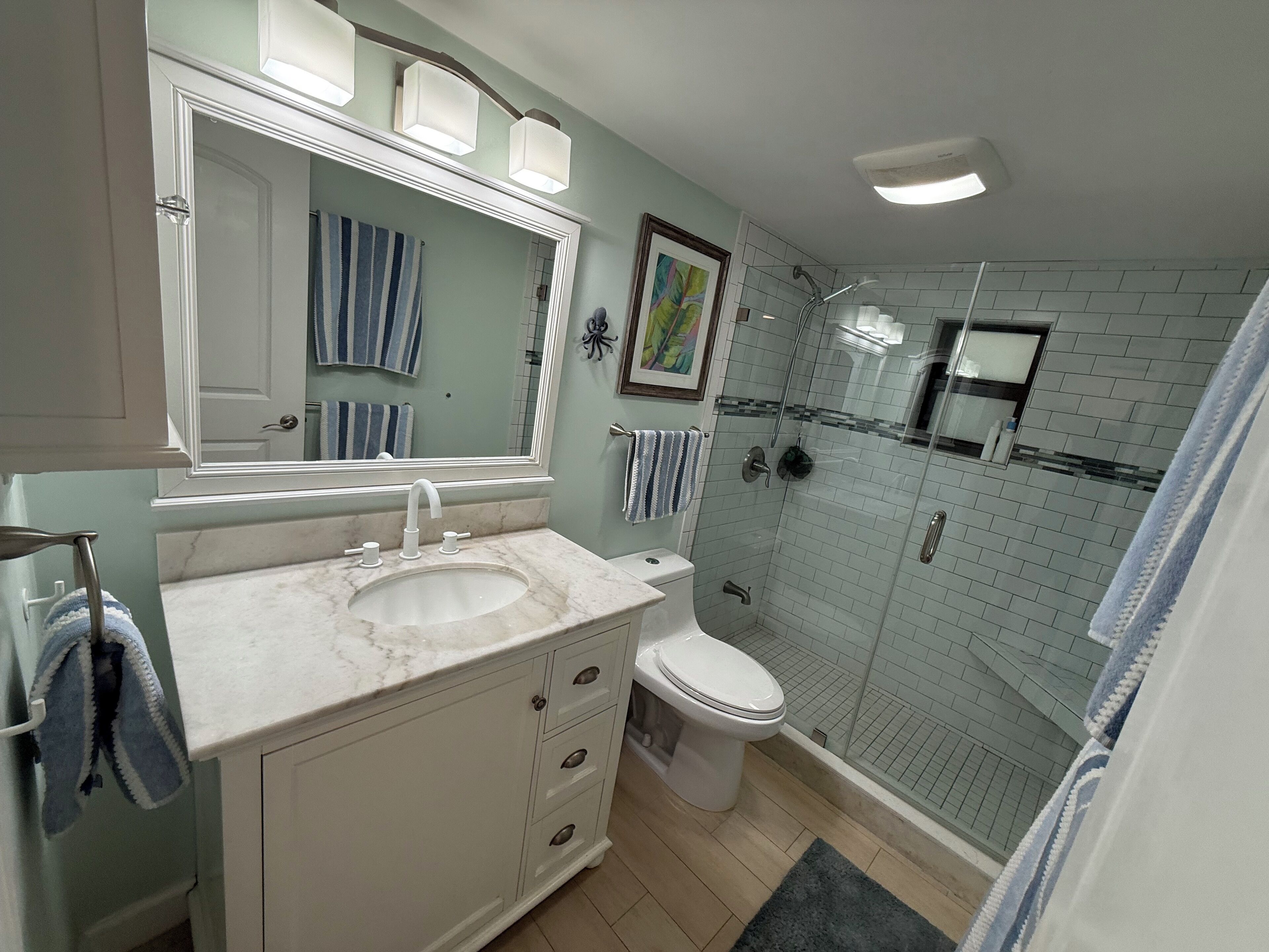 A bathroom with a white vanity, a large mirror, a shower enclosure, and a toilet.