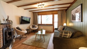 A living room with a fireplace, a television, a sofa, and a window with curtains. - Forest- finest selections (Zermatt)