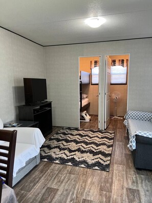 A hotel room with a bed, a desk with a TV, a small seating area, a rug, and a door leading to a bathroom.