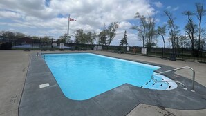 A rectangular swimming pool with a metal ladder, surrounded by a black fence, and a Canadian flag in the background.