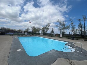 A rectangular swimming pool with a metal ladder, surrounded by a black fence, and a Canadian flag in the background.