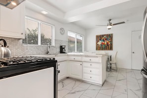 A modern kitchen with white cabinets, a gas stove, a coffee maker, and a dining area with a chair. - 5bed 3bath home with piano in Los Angeles by Universal studio & Hollywood-10 (Los Angeles)
