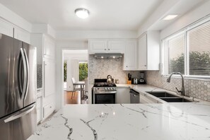 A modern kitchen with white cabinetry, a stainless steel refrigerator, a marble countertop, and a view of the outdoors through large windows. - 5bed 3bath home with piano in Los Angeles by Universal studio & Hollywood-10 (Los Angeles)