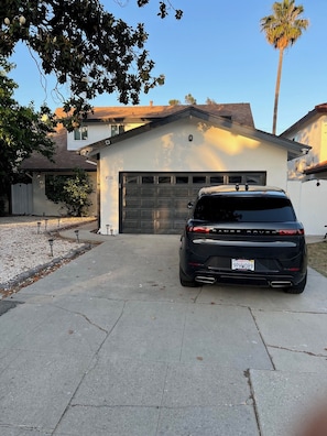A black SUV parked in a driveway with a garage door, a house with a white exterior, and a palm tree in the background. - 5bed 3bath home with piano in Los Angeles by Universal studio & Hollywood-10 (Los Angeles)