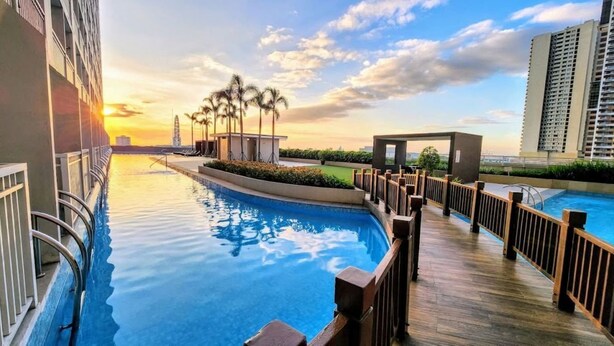 Une piscine avec une terrasse en bois, entourée de bâtiments et de palmiers, au coucher du soleil.