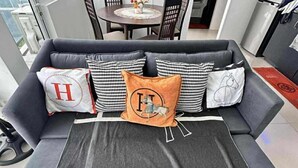 Un salon moderne avec un canapé gris, des coussins à motifs et un plaid décoratif placé au centre.