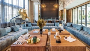 A spacious lounge area with a grand piano, comfortable seating, and a large window offering a view of the city.
