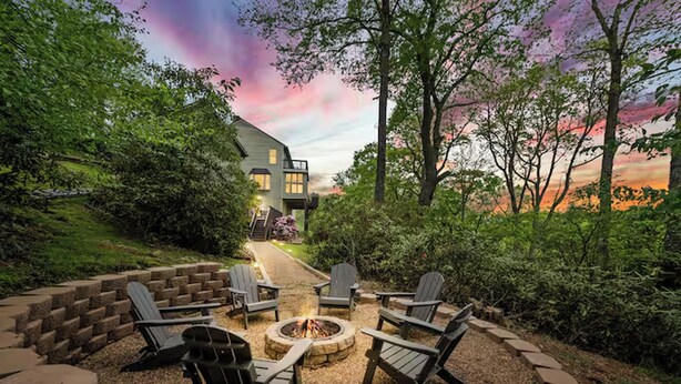 Een terras met Adirondack stoelen en een vuurkuil, omgeven door een stenen muur en weelderige begroeiing.