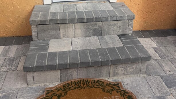 Une porte d’entrée avec une pancarte indiquant « NOUVEAU PRODUIT », un paillasson sur lequel est écrit « BIENVENUE CHEZ VOUS » et un mur orange à texture.