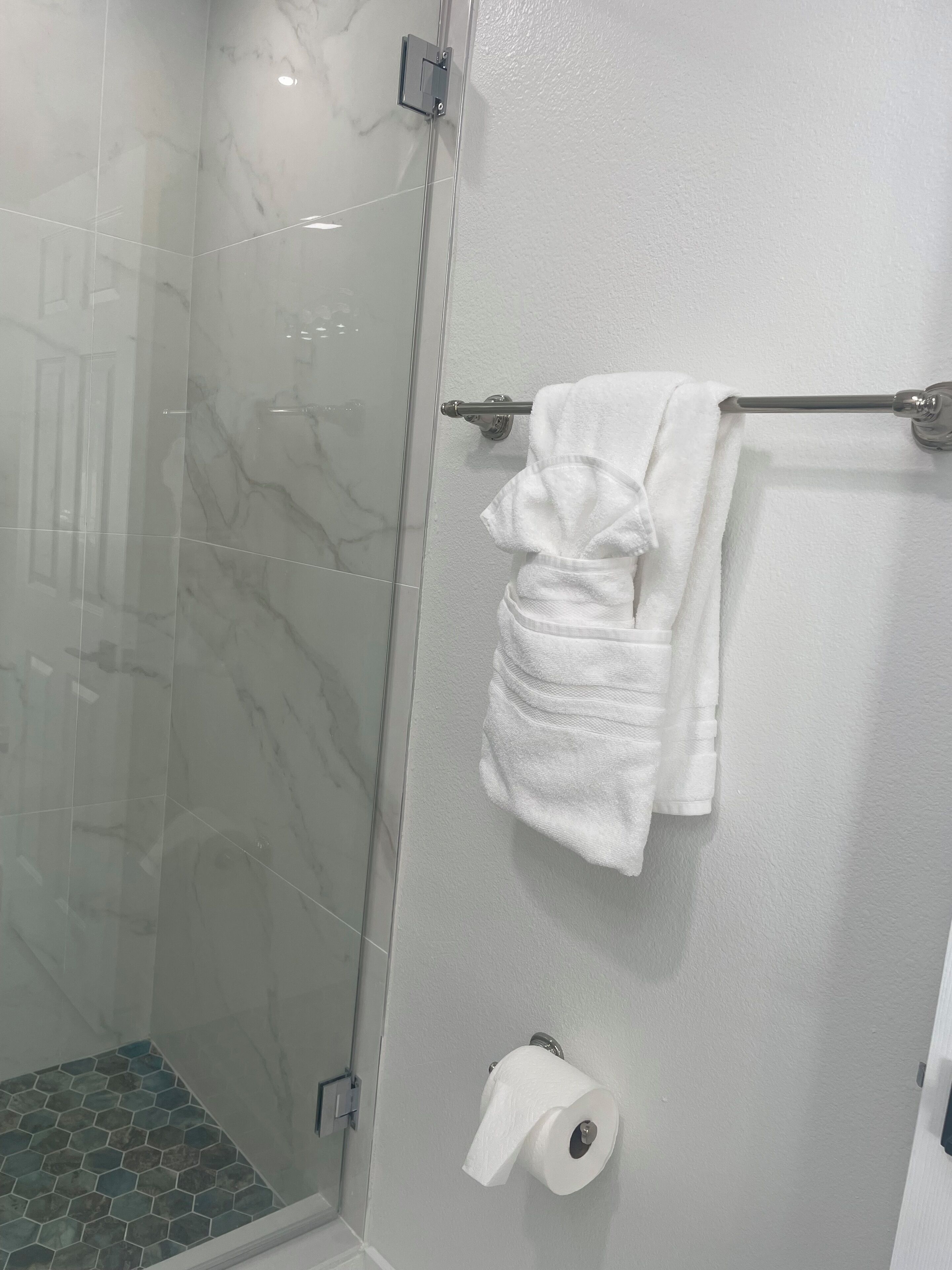 Une salle de bain avec une douche à parois de verre, un porte-serviettes blanc et un support à papier toilette.