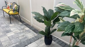 Une plante en pot, placée dans un pot noir, sur une terrasse carrelée.