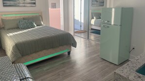 Une chambre à coucher avec un lit, un réfrigérateur à la porte verte et une porte-fenêtre coulissante donnant sur un balcon.