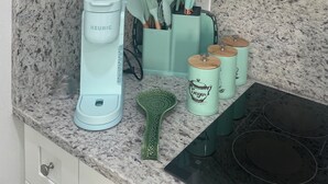Une cuisine dotée d’un plan de travail en granit, d’une machine à café Keurig, d’une spatule verte et d’un récipient à sucre.