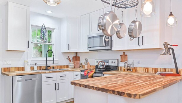 A modern kitchen with white cabinets, stainless steel appliances, and a wooden island. - Riverside Cottage just a short walk to downtown! (Bonita Springs)